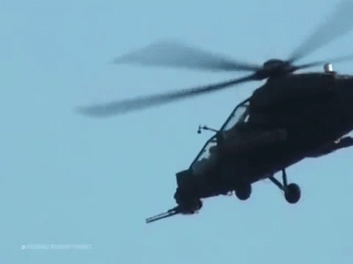 A Military Helicopter Is Flying In A Blue Sky . GIF