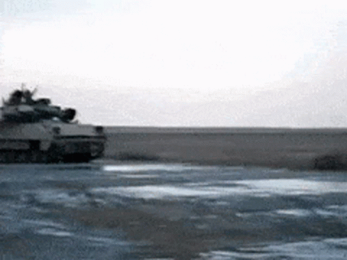 A Military Tank Is Driving Down A Dirt Road GIF
