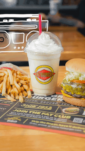 a milkshake from fatburger sits on a table with french fries and a hamburger