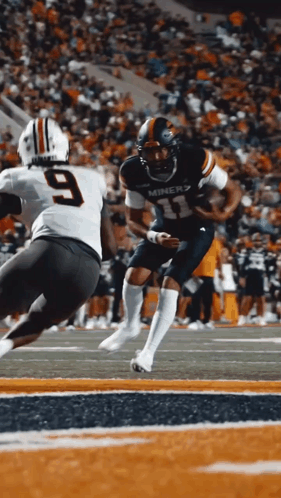 a miners football player runs with the ball as a player with the number 9 tries to tackle him