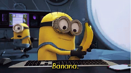 A Minion Holding A Banana In Front Of A Keyboard That Says Banana On It GIF