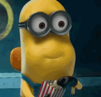 A Minion Wearing Goggles Is Holding A Bag Of Popcorn And A Chocolate Bar . GIF