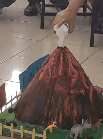 A Model Of A Volcano With A Sign That Says Eruption GIF