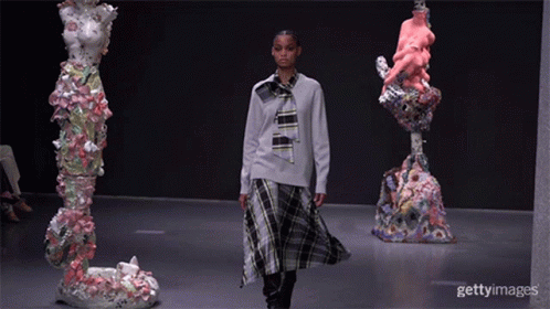 A Model Walks Down The Runway At A Fashion Show Surrounded By Sculptures GIF