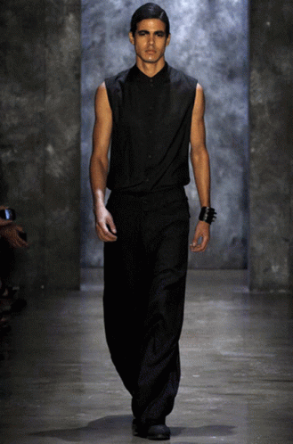 A Model Walks Down The Runway At A Fashion Show Wearing A Black Shirt And Black Pants GIF