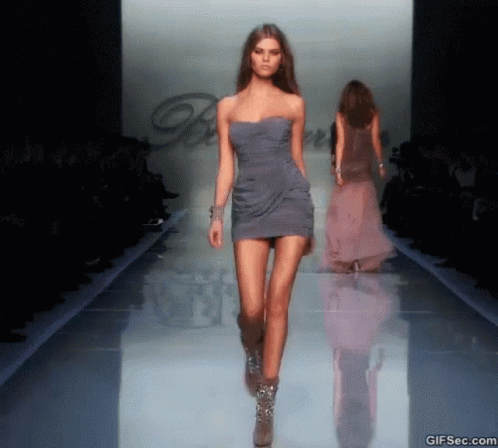 A Model Walks Down The Runway At A Fashion Show Wearing A Grey Dress GIF