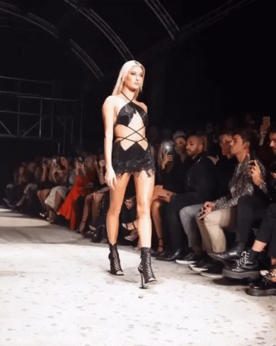 A Model Walks Down The Runway At A Fashion Show While A Crowd Watches GIF