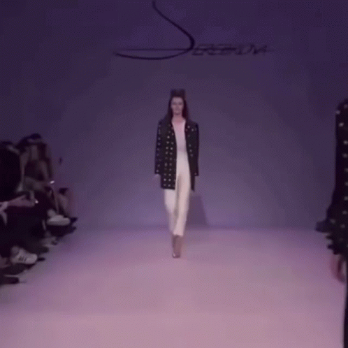A Model Walks Down The Runway At A Fashion Show With A Purple Background GIF