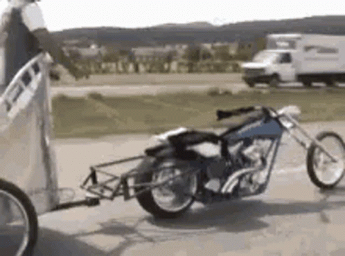 A Motorcycle Is Being Pulled By A Trailer On A Road . GIF