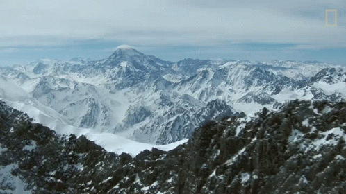 A Mountain Covered In Snow And Rocks With A Mountain In The Background GIF