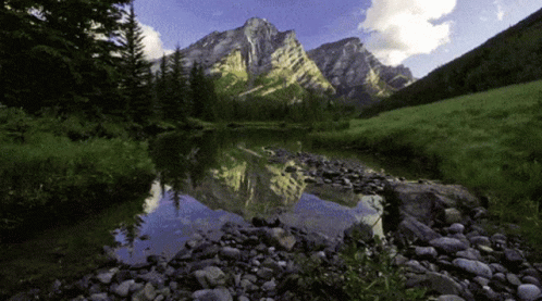 A Mountain Is Reflected In A Lake With Rocks In The Foreground GIF