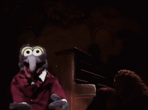 a muppet with big eyes and a red suit is sitting in front of a piano