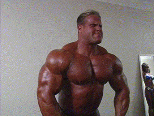 A Muscular Man Stands In Front Of A Mirror GIF