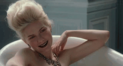 A Naked Woman Is Sitting In A Bathtub Wearing A Black Necklace And Smiling . GIF