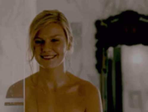 A Naked Woman Is Smiling In Front Of A Mirror In A Dark Room . GIF
