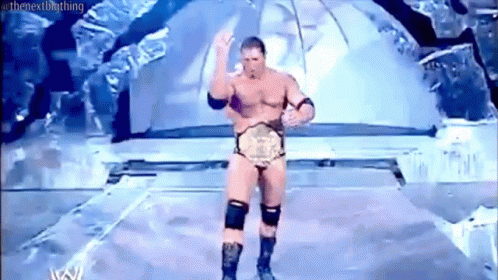 A Naked Wrestler Is Standing On A Stage With A Wrestling Championship Belt . GIF