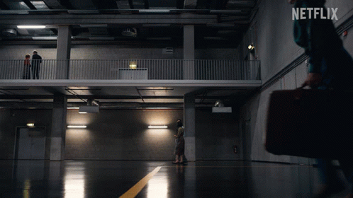 A Netflix Ad Shows A Woman Carrying A Briefcase Walking In A Dark Room GIF