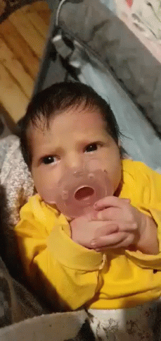 A Newborn Baby Is Holding A Pacifier In His Mouth . GIF