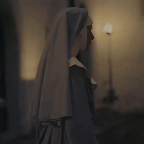 A Nun Is Standing In A Dark Room Wearing A White Veil GIF