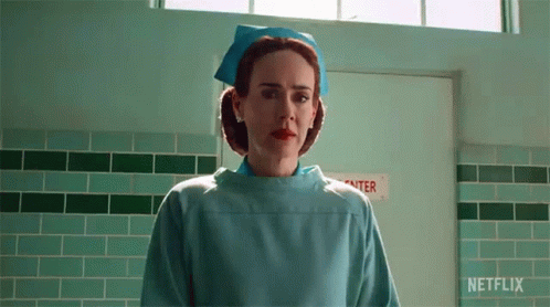A Nurse In A Blue Uniform Is Standing In A Hallway . GIF