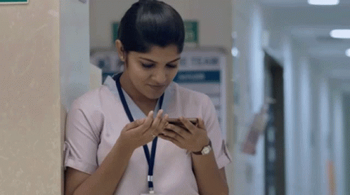 A Nurse Is Leaning Against A Wall And Looking At Her Phone GIF