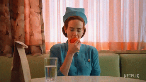 A Nurse Is Sitting At A Table With A Glass Of Water And An Apple In Her Mouth . GIF
