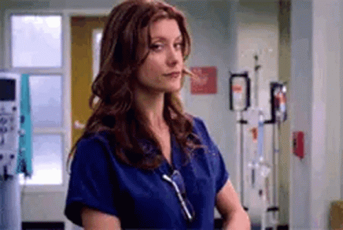A Nurse Is Standing In A Hospital Room Wearing A Blue Scrub Top . GIF