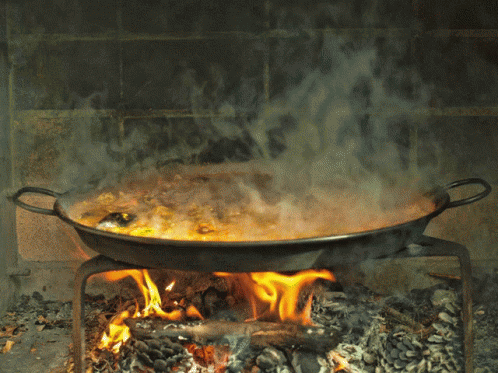 A Pan Of Food Is Cooking Over A Fire In A Fireplace GIF