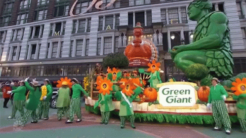 A Parade With A Green Giant Float In The Middle GIF