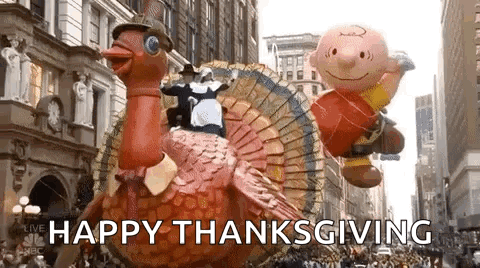 A Parade With A Turkey Float And Charlie Brown Balloons Flying In The Air . GIF