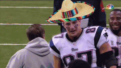 A Patriots Player Wearing A Sombrero Is Talking To A Man GIF