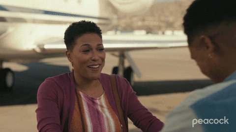 A Peacock Ad Shows Two Women Talking In Front Of A Plane GIF
