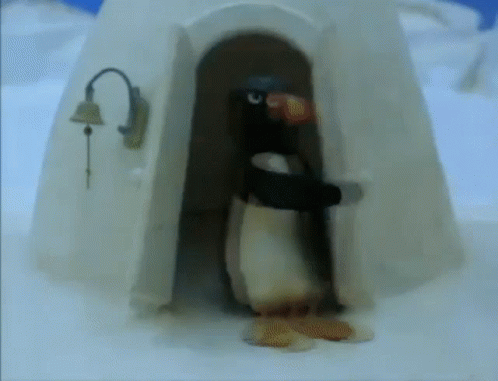 A Penguin Standing In Front Of An Igloo With A Bell On It GIF