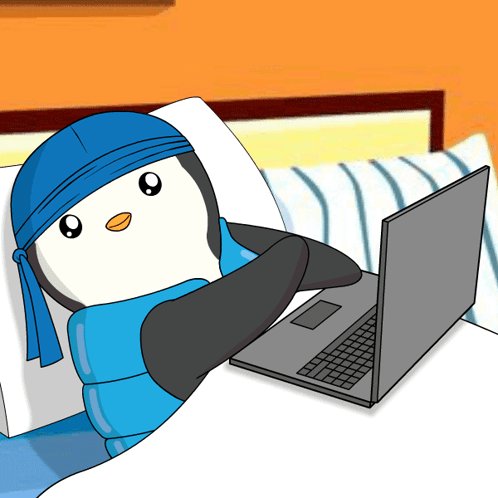 A Penguin Wearing A Blue Bandana Is Laying On A Bed Next To A Laptop GIF