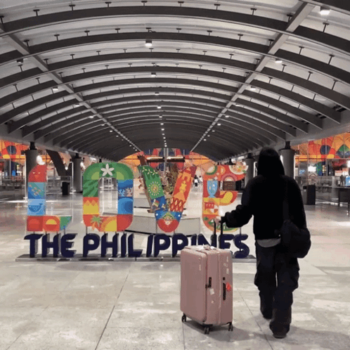 A Person Carrying A Suitcase Walking In Front Of A Sign That Says The Philippines GIF