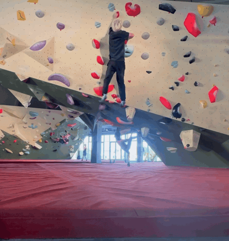 A Person Climbs A Climbing Wall With A Red Mat GIF