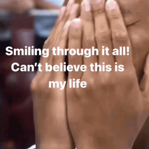 A Person Covering Their Face With Their Hands With The Words Smiling Through It All GIF