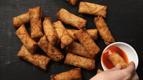 A Person Dipping A Fried Egg Roll In A Bowl Of Sauce GIF