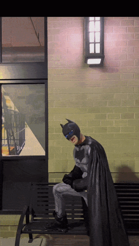 A Person Dressed As Batman Sits On A Bench GIF