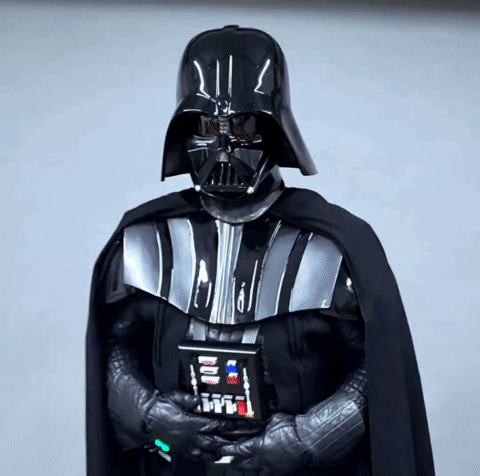 A Person Dressed As Darth Vader Holds A Remote Control In His Hand GIF