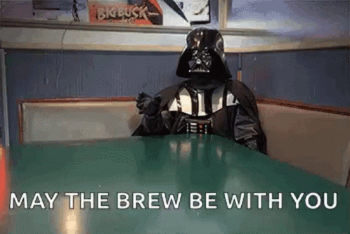a person dressed as darth vader is sitting at a table in a diner and saying `` may the brew be with you ''