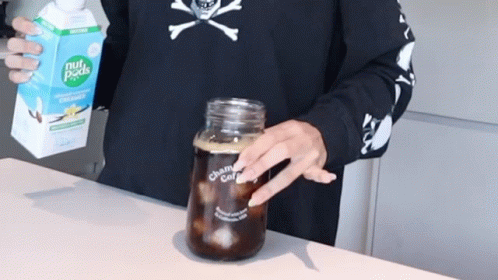 A Person Holding A Carton Of Nut Pods Next To A Jar Of Coffee GIF
