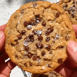 A Person Holding A Chocolate Chip Cookie With Sea Salt On Top GIF
