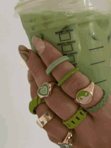 A Person Holding A Cup Of Green Tea With A Lot Of Rings On Their Hands GIF