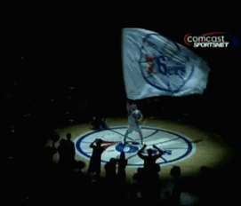 A Person Holding A Flag With A Comcast Logo On The Bottom Right GIF