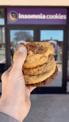 A Person Holding A Stack Of Cookies In Front Of An Insomnia Cookies Store GIF