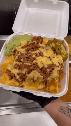 A Person Holding A Styrofoam Container Filled With Nachos Guacamole And Cheese GIF