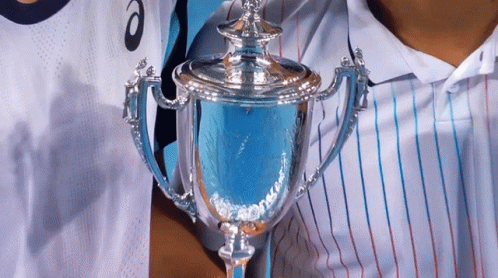 A Person Holding A Trophy In Front Of A Person Wearing A Shirt That Says Asics GIF