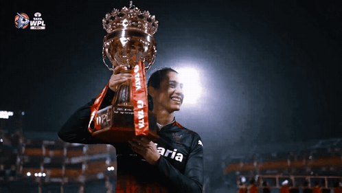 A Person Holding A Trophy With The Word Aria On Their Shirt GIF