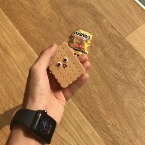 A Person Holding An Airpod Case In The Shape Of A Cookie Next To A Haribo Bag GIF